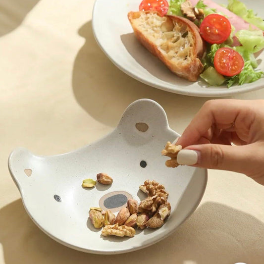 Person placing walnuts into a small white dish with a cat face design, next to a plate of salad.
