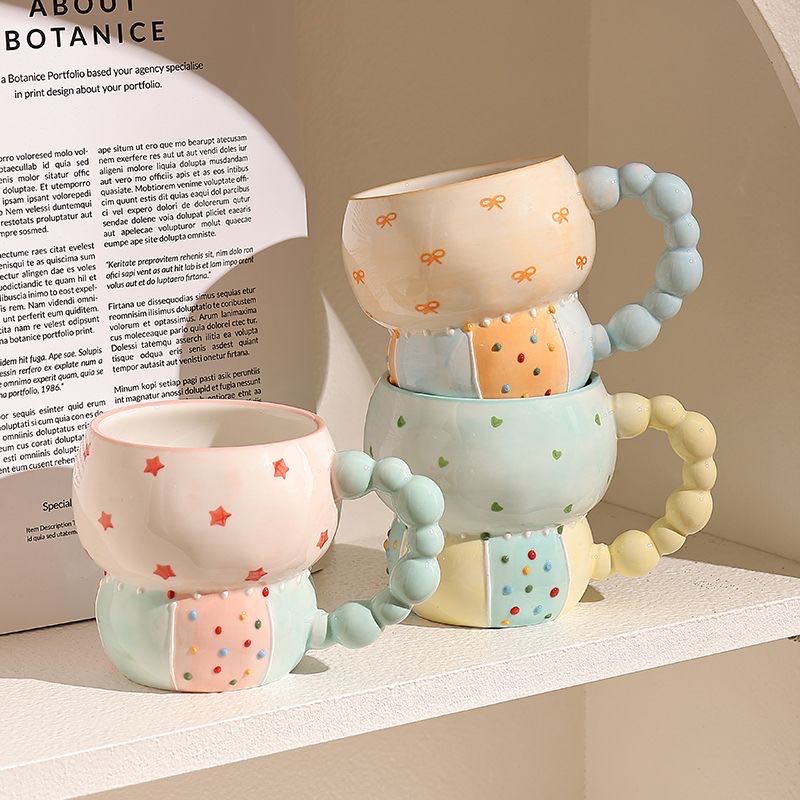 Three ceramic mugs with colorful designs on a surface with a blurred text background
