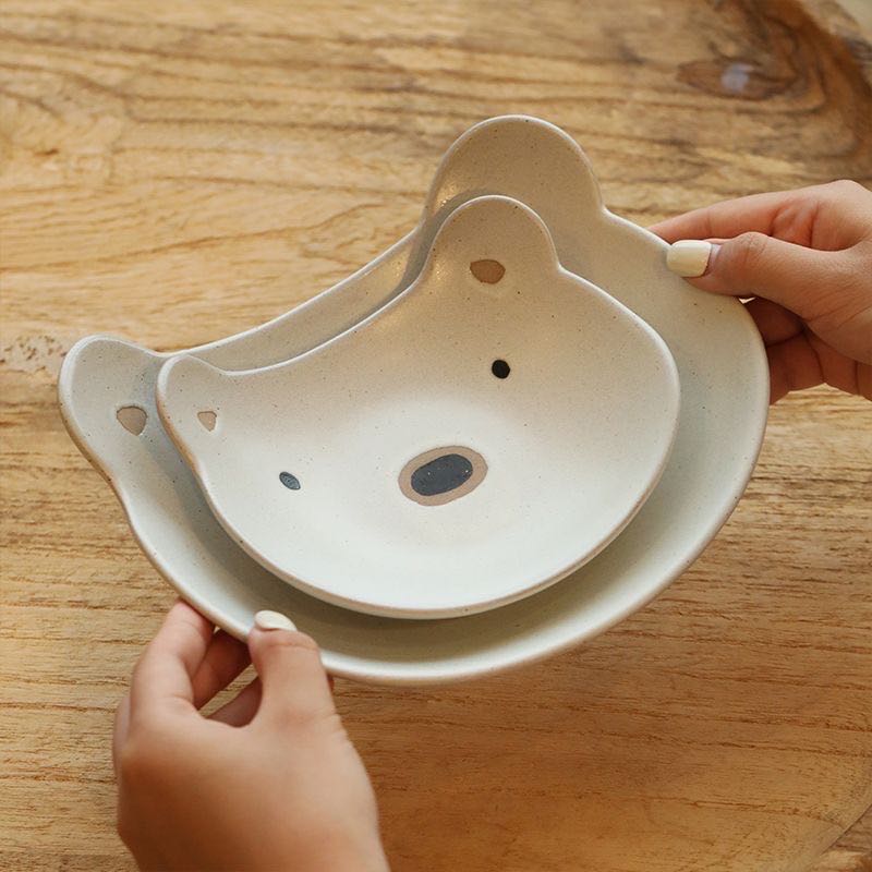 Ceramic bowl shaped like a bear with hands holding it on a wooden surface