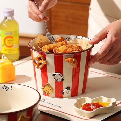Red and white striped bucket with fried chicken and snacks on a table with a bottle of juice in the background.