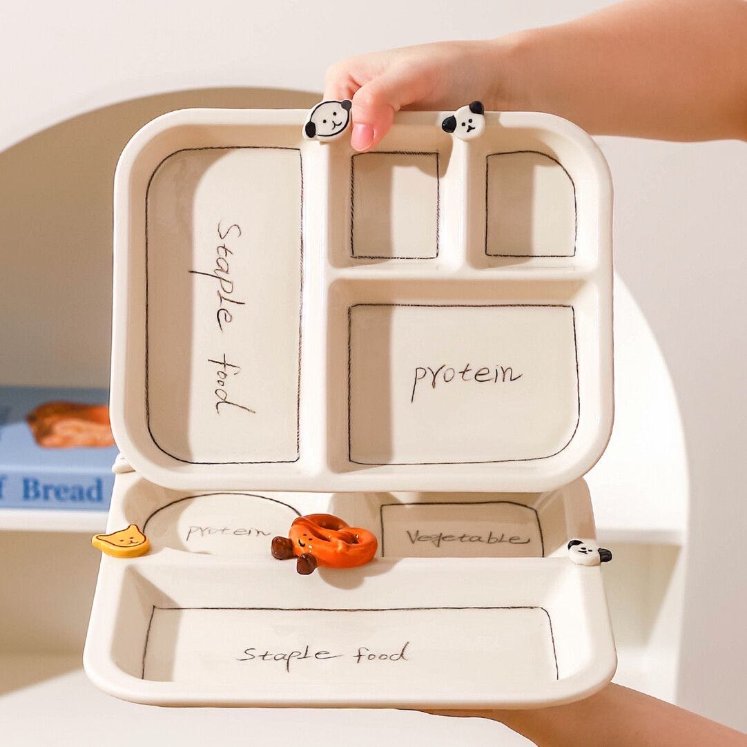 Divided food container with labels for staple food, protein, and vegetables, held by a hand.