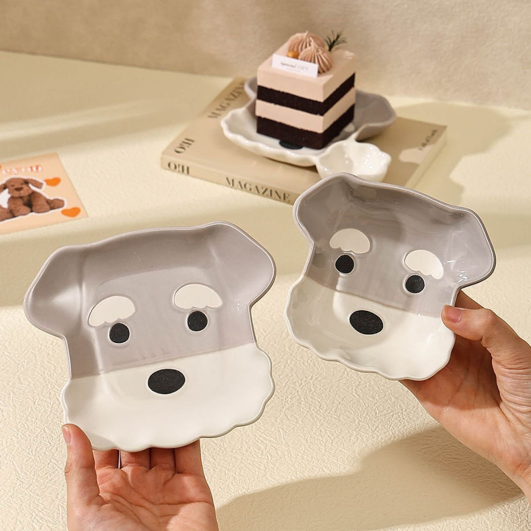 Two dog-shaped bowls held by hands with a piece of cake on a magazine in the background.