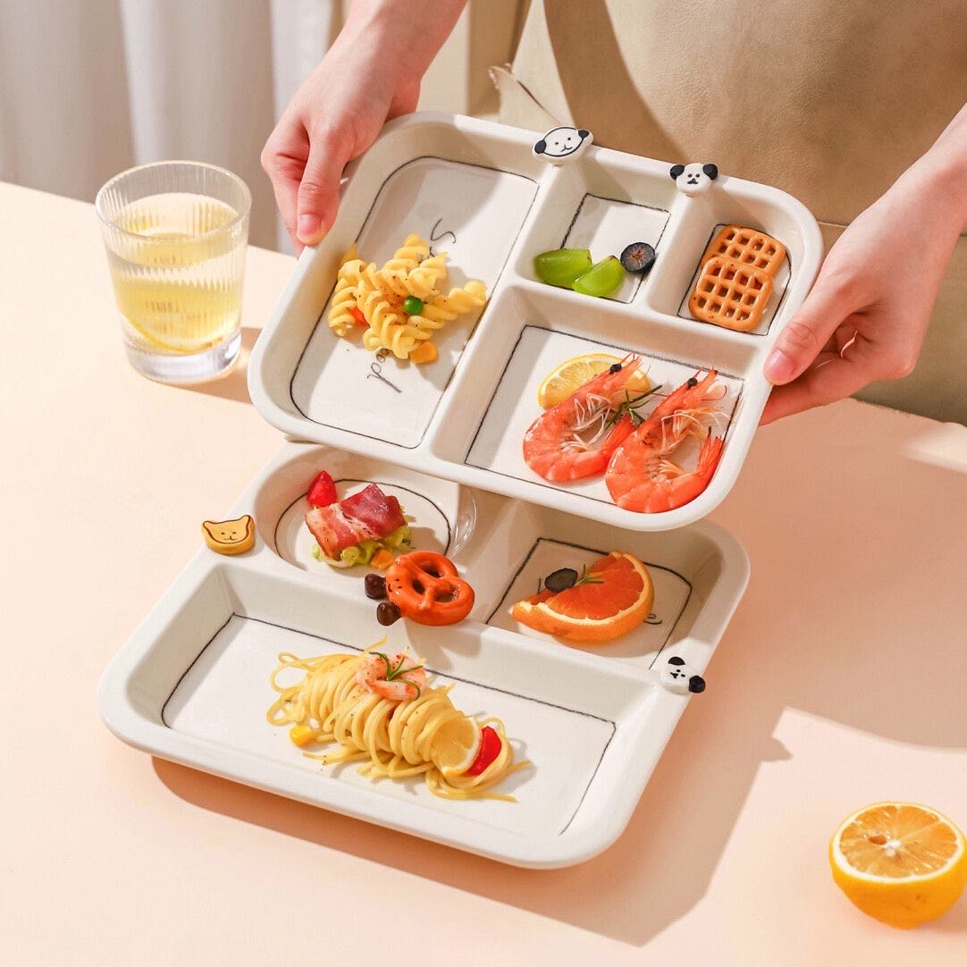 Person holding a white divided plate with various food items on a light surface.