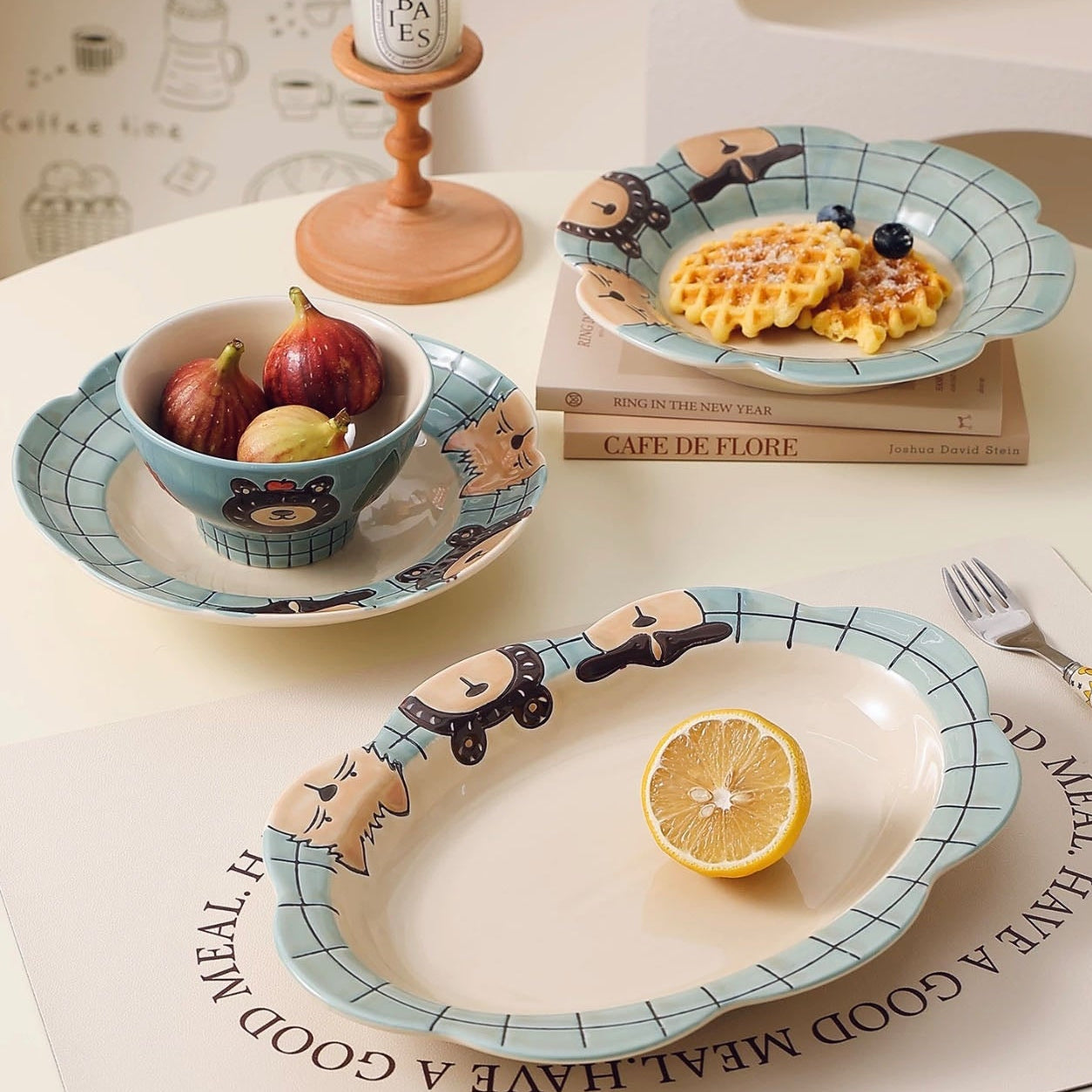 Ceramic plates with cartoon designs on a table with fruit and books.