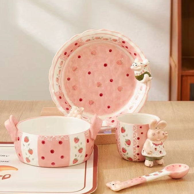 Cute ceramic tableware set with strawberry design on a wooden surface.