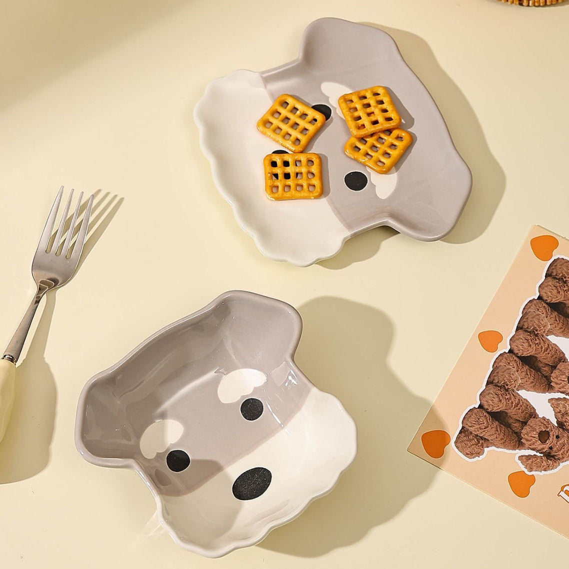 Two ghost-shaped plates with waffles on a beige surface, next to a fork and a box of teddy bear-shaped cookies.