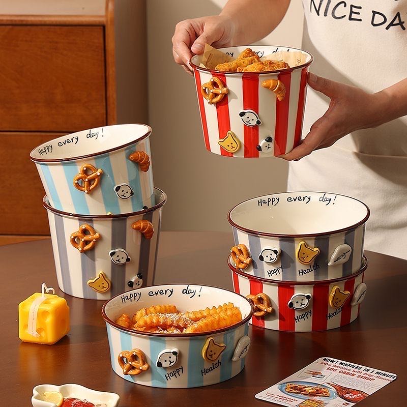 Person holding a striped popcorn bucket with cartoon characters, surrounded by similar buckets on a table.