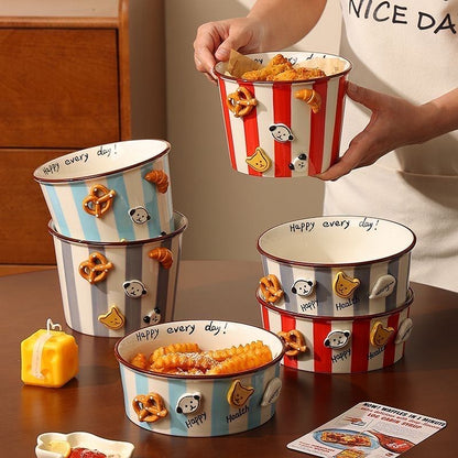 Person holding a striped popcorn bucket with cartoon characters, surrounded by similar buckets on a table.