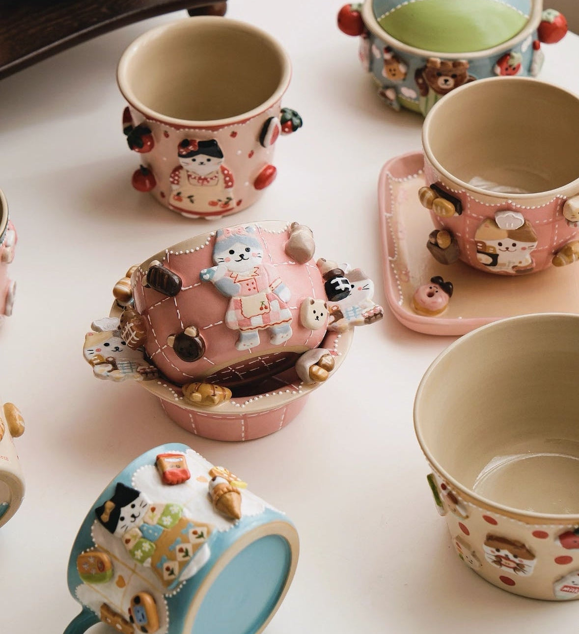 Set of cute, cartoon-style ceramic cups and saucers on a white surface.