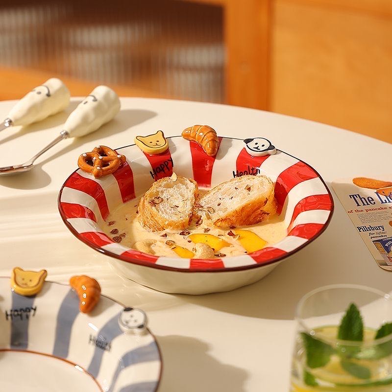 Ceramic bowl with cartoon designs on a table with a magazine and glass.