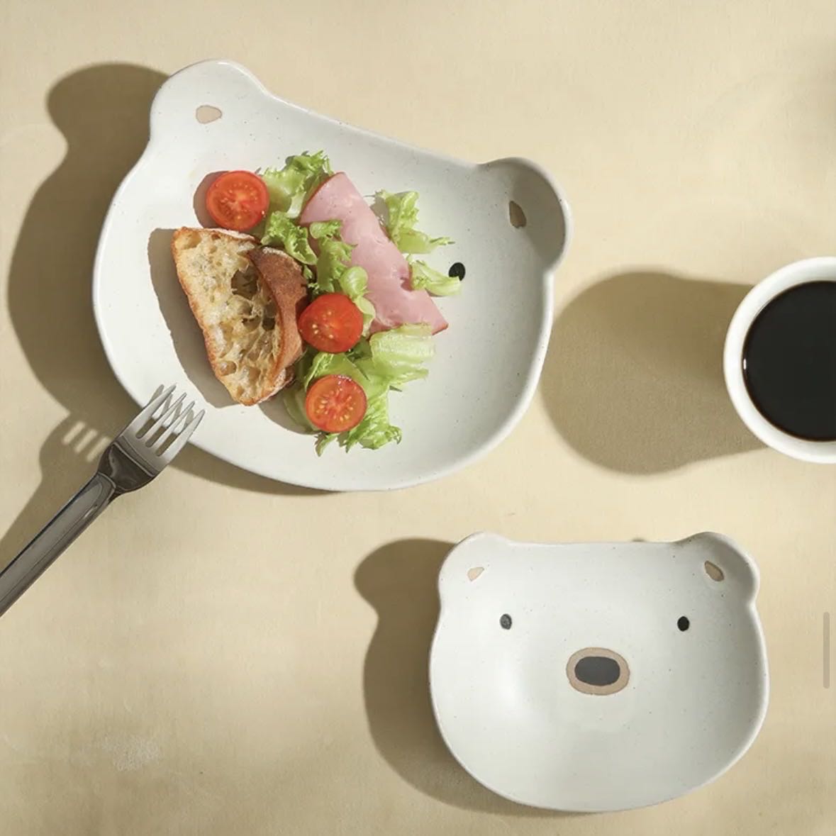 Bear-shaped plate with a salad and bread, accompanied by a bear-shaped bowl and cup on a beige background.