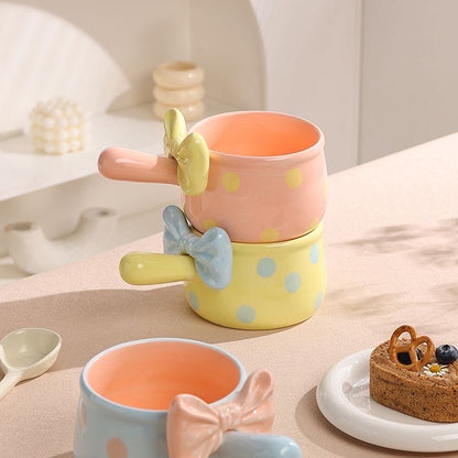 Set of colorful ceramic mugs with bow designs on a table with a dessert.