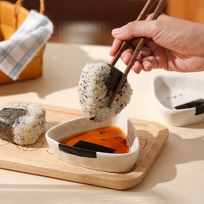 Person dipping a sushi ball into soy sauce using chopsticks on a wooden board.