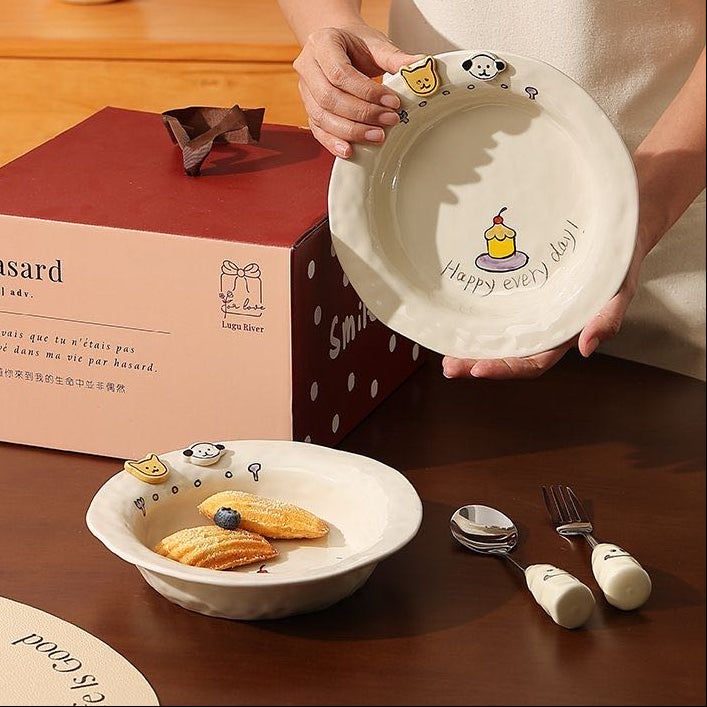 Person holding a ceramic plate with cartoon designs on a wooden table with a box labeled 'Hasard' in the background.