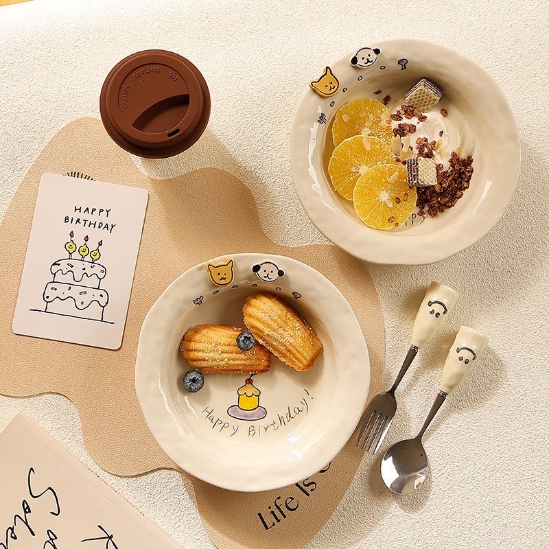 Two ceramic plates with food and cutlery on a textured surface, featuring 'Happy Birthday' and 'Life is Sweet' text.