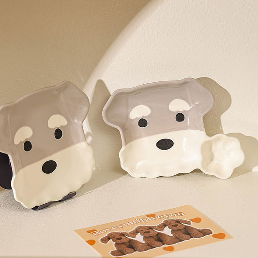 Two dog-shaped bowls with a card featuring dog illustrations on a beige surface.