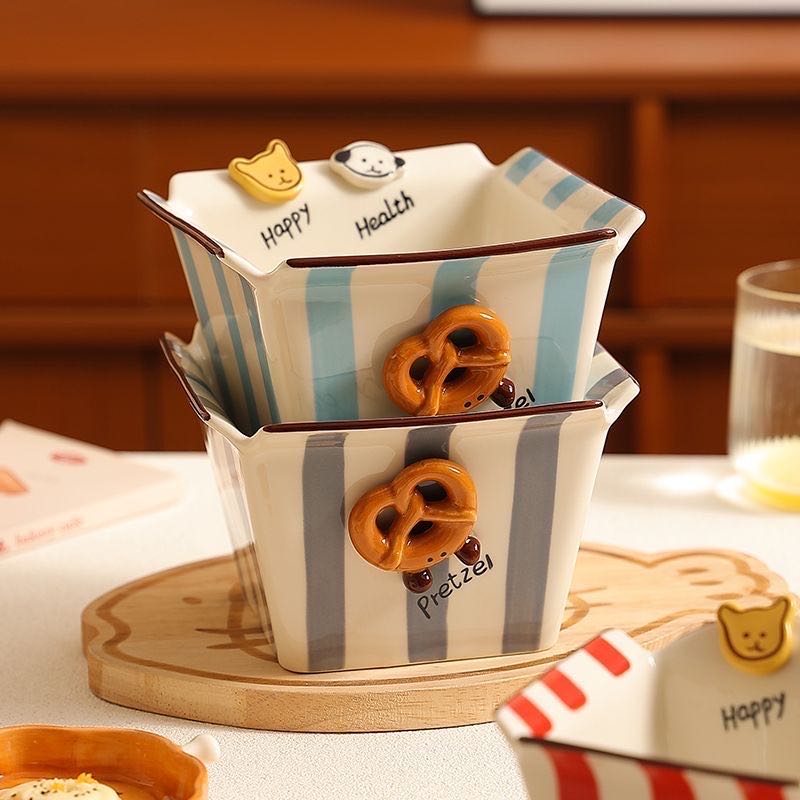 Stackable ceramic containers with striped design and pretzel decorations on a wooden surface.
