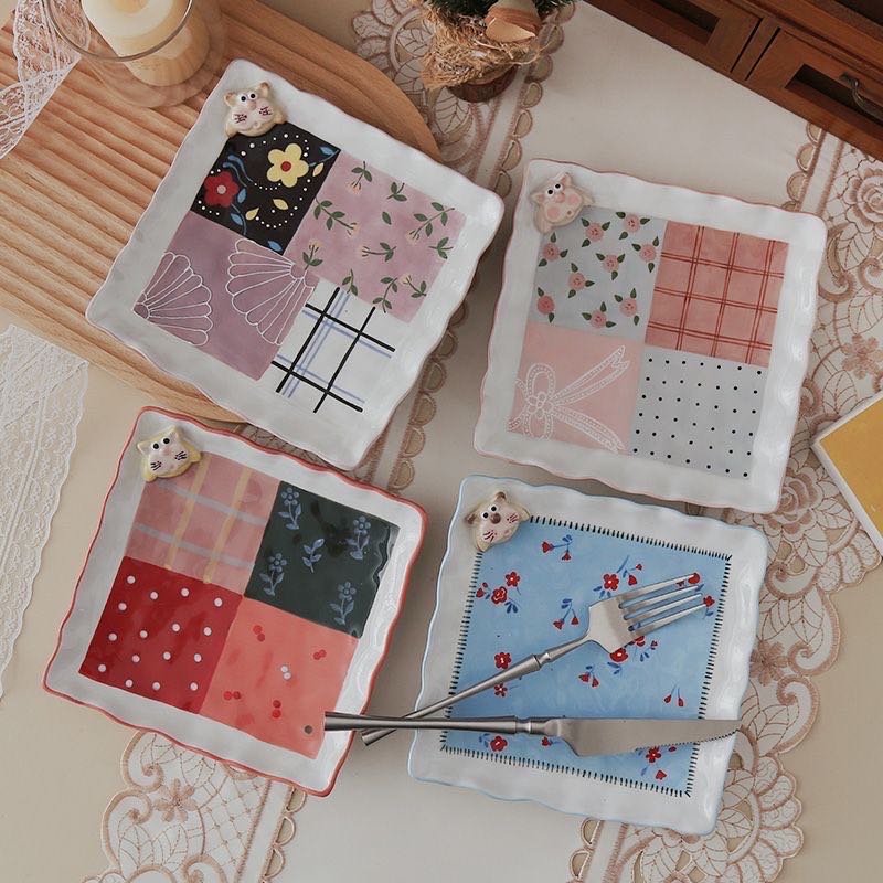 Set of decorative square plates with various patterns on a lace tablecloth.