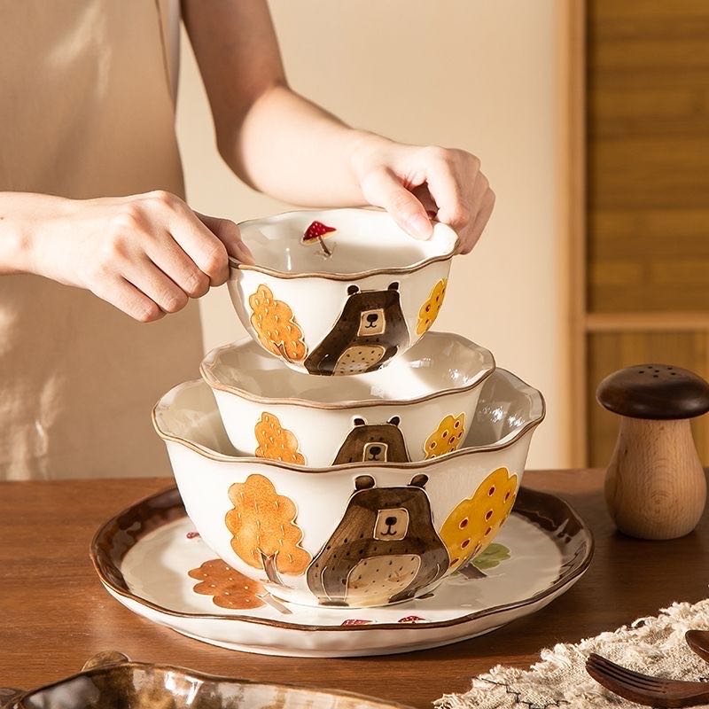 Stack of ceramic bowls with bear and flower design on a wooden table.