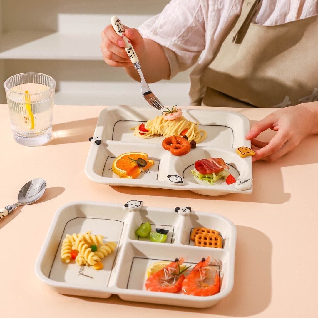 Children's divided plate with cartoon designs filled with food, held by a person.