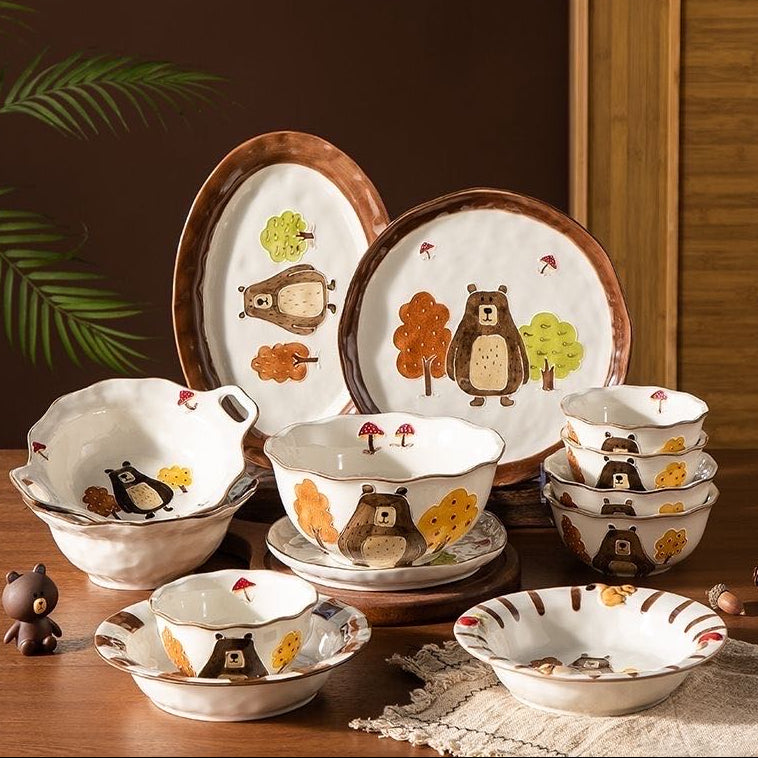Set of ceramic dishes with bear and forest design on a wooden table.