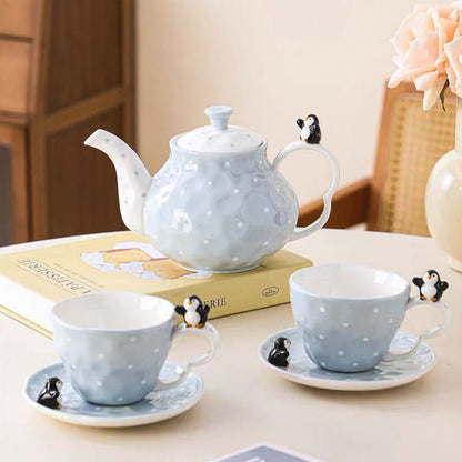 Tea set with teapot, cups, and saucers on a table with a floral arrangement in the background.