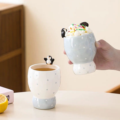 Two ceramic mugs with penguin decorations on a light surface.